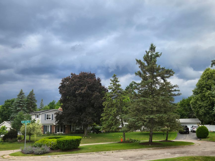 Suburban neighborhood with lush greenery under dramatic storm clouds, creating a moody atmosphere.
