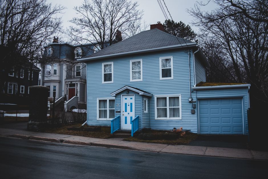 Exterior of small residential house trimmed with light blue wooden panels with white door and adjoin garage